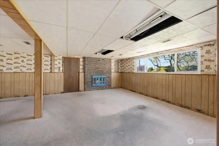 Wide open living room/rec room in the lower level of the main home, complete with wood burning fireplace and exterior door to carport