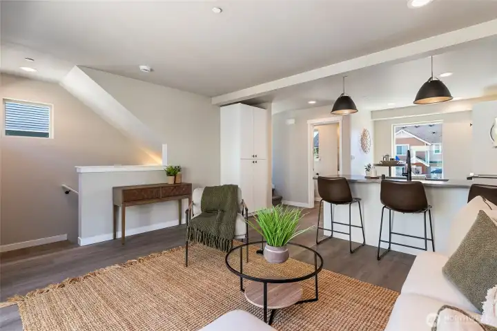Staged photo of like unit. Living/Kitchen area and stair landing with pantry in center of frame.