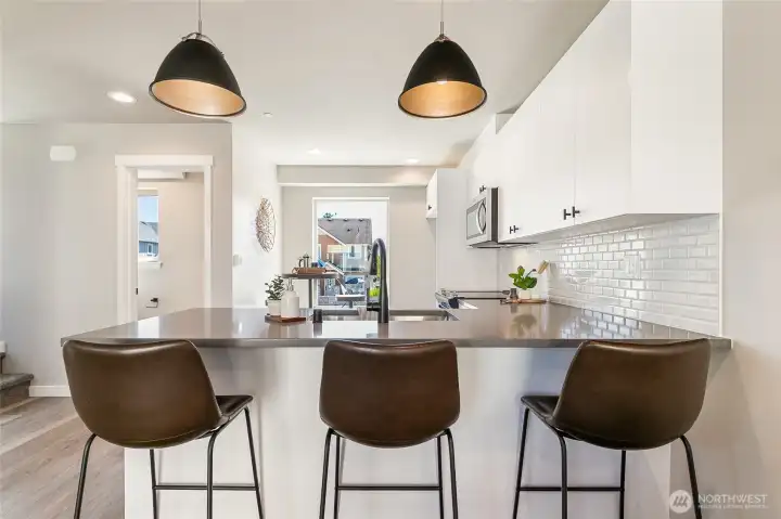 Staged photo of like unit. Stylish pendant lights round out this tasteful kitchen