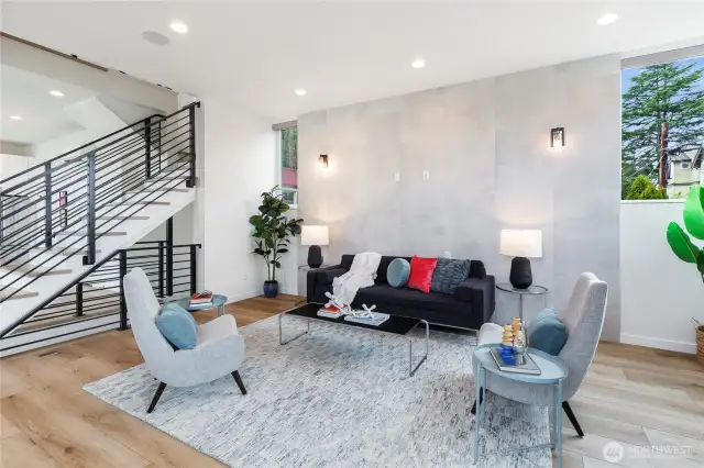 Generously sized second level living room with tall ceilings, dramatic center staircase, large format porcelain tile accent wall, Oak plank flooring, territorial views, air conditioning and great light.