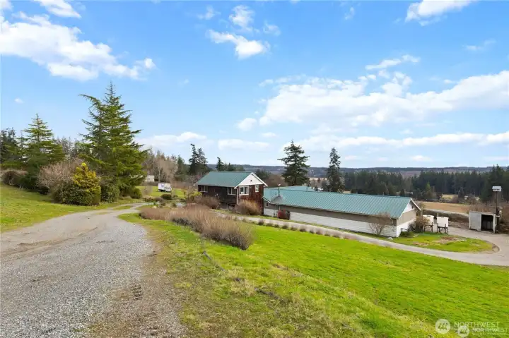 This peaceful country property features a charming home with a green metal roof, multiple outbuildings, and sweeping territorial views on a spacious lot.
