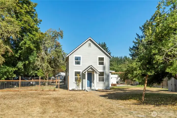 A welcoming stone pathway leads to the front entrance, framed by colorful plantings that add charm and character. The fully fenced side yard on the left provides extra space for gardening, pets, or play..