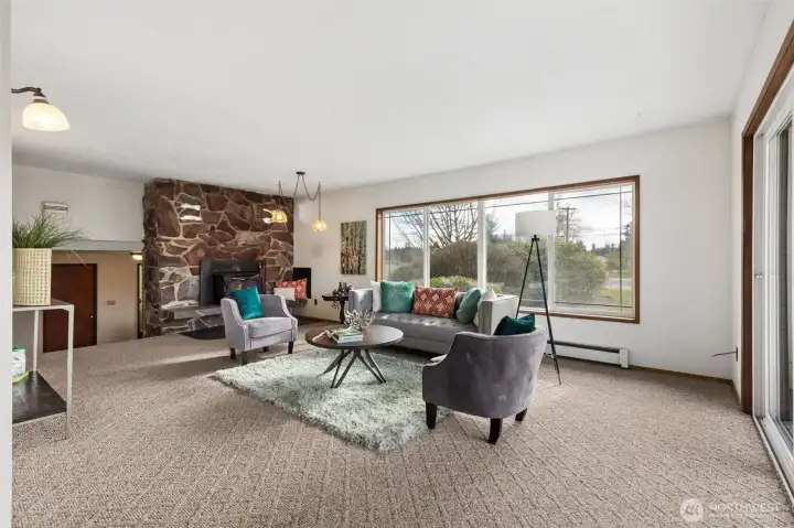 This is another view of the living room showing rock fireplace wall. Look closely at the rock wall toward the top, there are two sets of lights!  With the split level and featured rock wall, it's truly a nod to the mid-century modern era! Baseboard heaters with circulated water throughout home fueled by an oil furnace. NOTE: The baseboard is NOT an electric heater, so it's okay to place furniture there. To the left of fireplace are the steps that lead down to the main entry. The living room is open to the dining room.