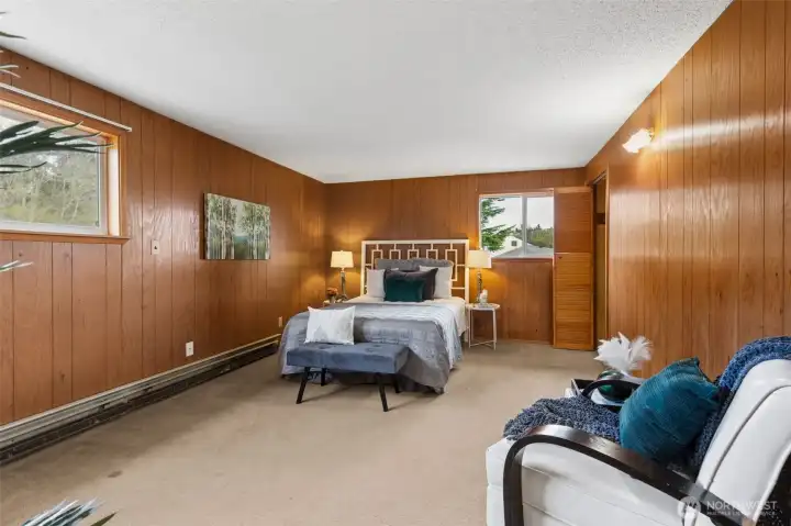 This is the primary bedroom (located on the 2nd floor) featuring wood-paneled walls offering a warm relaxed environment, a true nod to the mid century era this home was constructed. With the current heating system (hydronic baseboard) it's a soft heat allowing different options for furniture placement in this home. There are two windows that offer views to the back yard. The closet on the right is the smaller of two closets. Carpeted flooring. There is a 3/4 ensuite bathroom to the left.