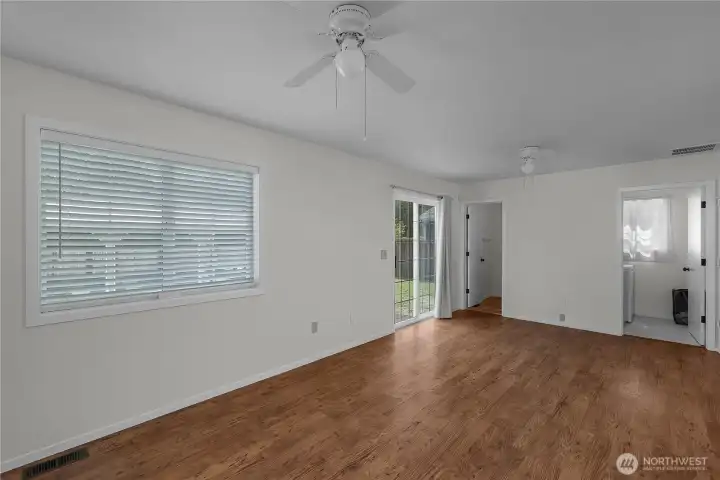Spacious family room with wood-style flooring, ceiling fans, large window, and sliding door to the yard.
