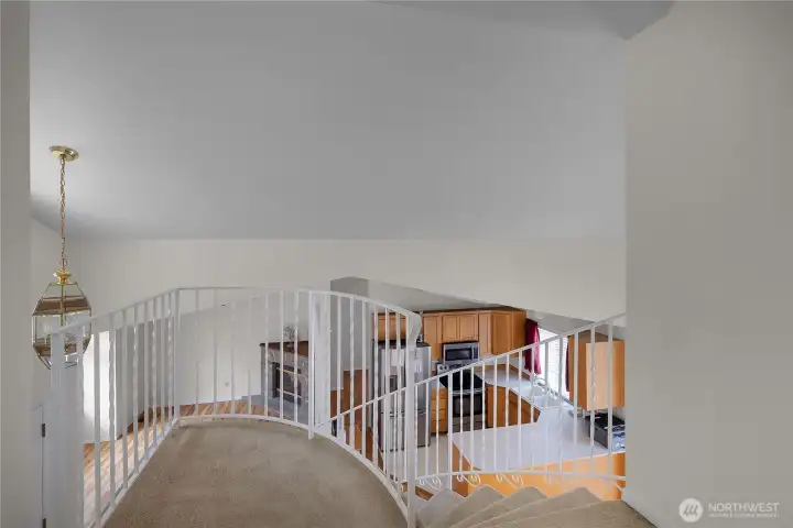 Upper landing with curved railing, carpeted stairs, and views toward the kitchen and living room.