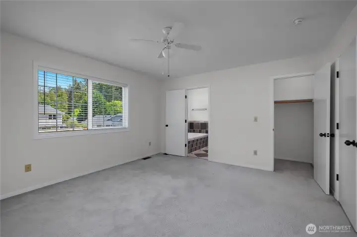 Primary bedroom with attached bath access, multiple closets, ceiling fan, and large window.