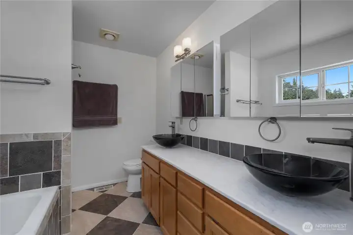 Updated primary bath with dual vessel sinks, long vanity, tile accents, and mirrored cabinetry.