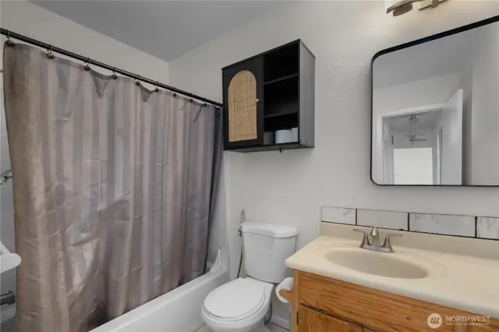 Hall Bath - Full bathroom with tub/shower, vanity, tile backsplash accent, and black-framed mirror.