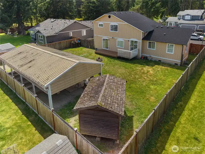 Aerial backyard view with detached 4-car carport, deck, storage shed, and full fencing.