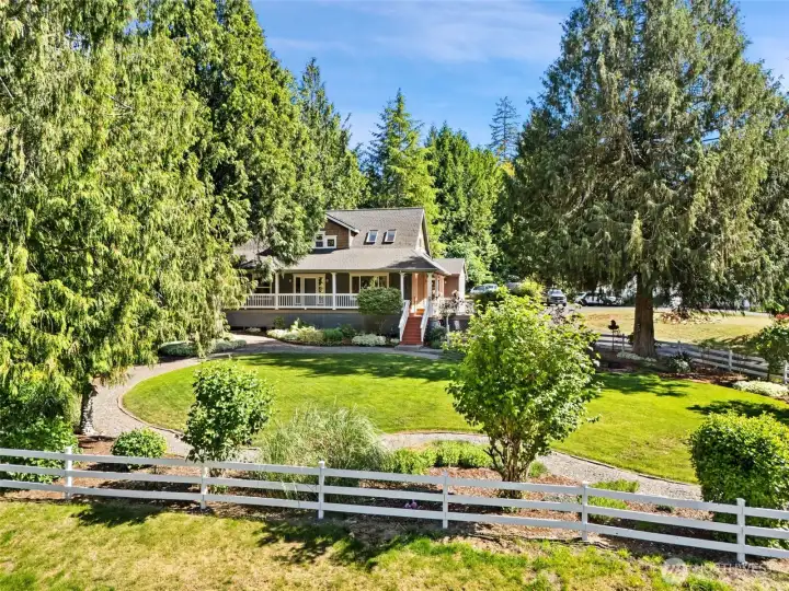 Welcome home to this picture-perfect PNW retreat! A beautifully manicured, expansive green lawn is framed by mature, towering evergreens and a classic white picket fence.