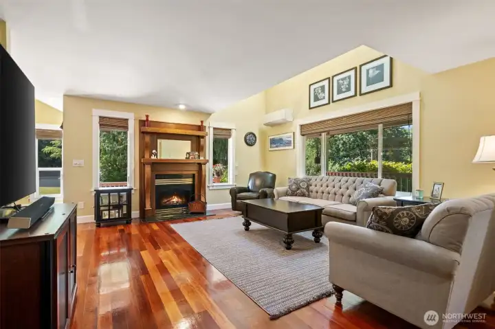 The heart of the home features an impressive living room anchored by a stunning, custom wood-mantel fireplace. Vaulted ceilings and massive picture windows flood the space with natural light and offer peaceful views of the surrounding greenery, while a mini-split system ensures year-round climate comfort.