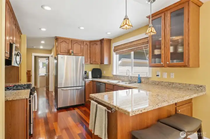 This functional, beautifully appointed kitchen features expansive granite countertops, rich oak cabinetry, and updated stainless steel appliances. The multi-level peninsula includes seating for casual dining under elegant pendant lights