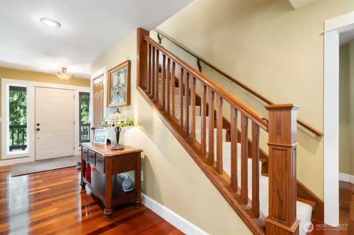 An elegant, solid wood staircase with a classic box newel post leads from the main foyer to the home’s upper level. The plush, neutrally carpeted stairs provide a quiet transition, while the rich hardwood floors and warm wall tones maintain a cohesive design language throughout the entryway.
