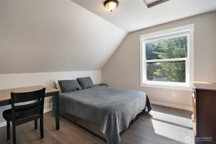 This cozy upper-level bedroom features a charming sloped ceiling that creates a snug, inviting atmosphere. Hardwood-style flooring adds a modern touch, while the large picture window