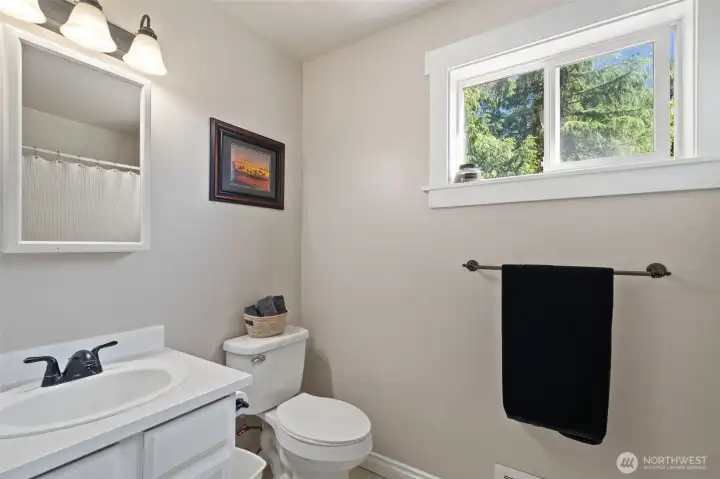 This crisp secondary bathroom features a well-maintained single vanity, neutral tone-on-tone walls, and a large slider window that provides excellent ventilation and natural light.
