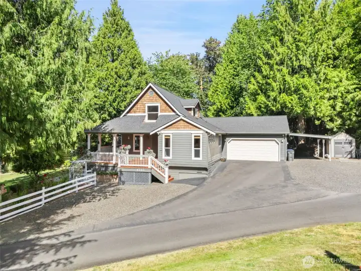 This eye-catching front perspective highlights the home’s exceptional architectural appeal. Combining classic grey siding with warm cedar shake accents, the residence features a spacious two-car garage, an adjacent gravel parking area perfect for a boat or RV
