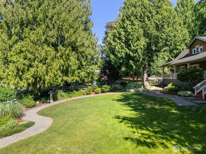 Looking back toward the residence, this angle emphasizes the home's idyllic setting. The deeply curved gravel path serves as both a practical walkway and a beautiful design element, connecting the lower yard to the main porch stairs while maximizing the visual flow of the lush outdoor space.