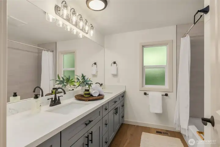Beautifully remodeled to reflect the home's contemporary style, the spacious main-level bathroom features a long quartz vanity with custom cabinetry, designer lighting, matte black fixtures, and a full tub with a sleek tiled surround. Beautifully remodeled to reflect the home's contemporary style, the spacious main-level bathroom features a long quartz vanity with custom cabinetry, designer lighting, matte black fixtures, and a full tub with a sleek tiled surround.