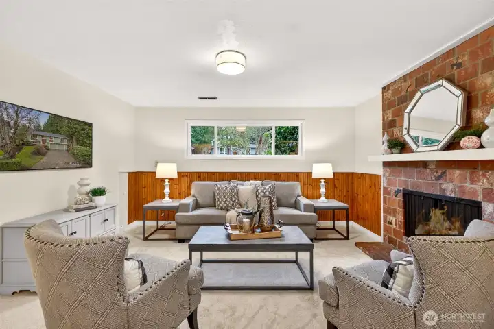 This cozy rec room sets the tone for relaxed evenings, with plush carpeting underfoot and a classic brick fireplace that instantly makes the space feel warm and inviting. The rich wood wainscoting adds character and texture, while the wide picture window brings in soft natural light and greenery views. It is the kind of room you will actually use, perfect for movie nights, game day, or a quiet spot to unwind by the fire.