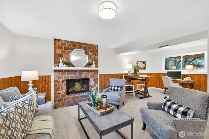 This angle shows just how versatile the lower level is, offering plenty of room to spread out with a comfortable lounge area anchored by the brick fireplace and crisp white mantle. The wood wainscoting wraps the space in a classic, Northwest feel, and the open layout easily supports multiple zones. You can entertain, relax, and still have space for hobbies or a work area, all in one welcoming room.