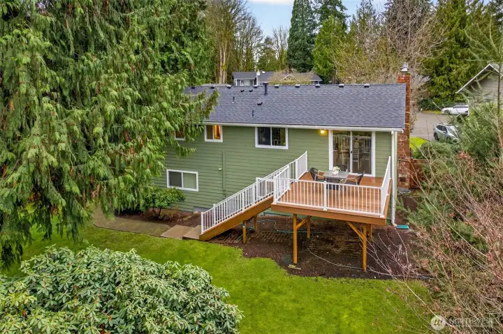An elevated view captures the home’s privacy and green surroundings, with the deck perched above the yard. The combination of mature trees, fenced boundaries, and updated exterior presence creates a calm retreat feel.