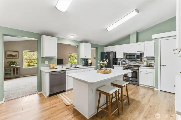 The kitchen has a stainless steel dishwasher, range and refrigerator, along with slab quartz counters and white cabinets.