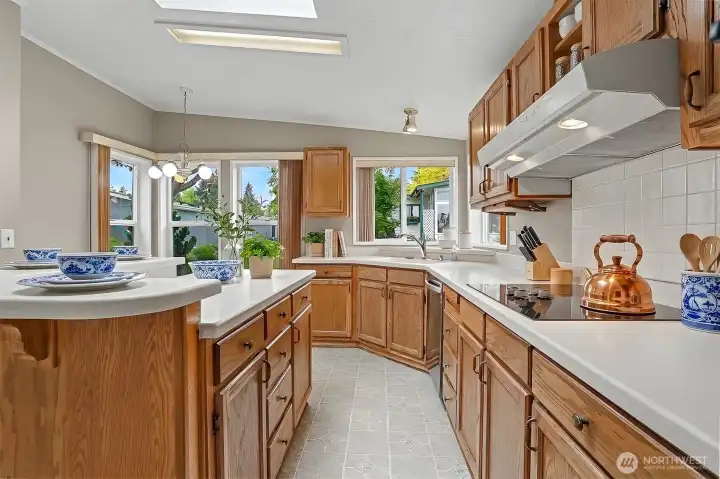Gourmet kitchen features a center island, quartz counters, skylight, oak cabinets, wall oven, cooktop and a eating nook overlooking the community greenbelt.  Virtually staged photo.