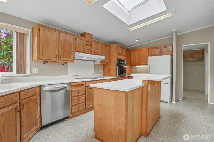 Gourmet kitchen features a center island, quartz counters, skylight, oak cabinets, wall oven, cooktop and a eating nook overlooking the community greenbelt.