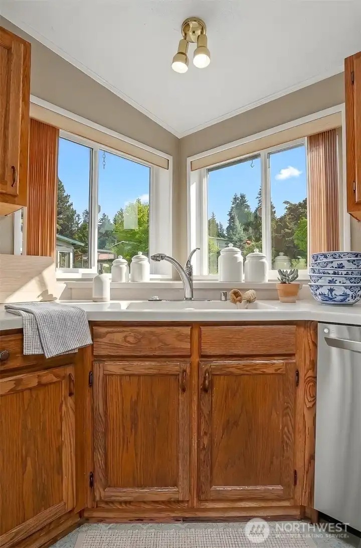 Gourmet kitchen features a center island, quartz counters, skylight, oak cabinets, wall oven, cooktop and a eating nook overlooking the community greenbelt.  Virtually staged photo.