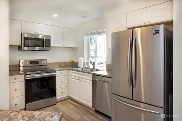 Kitchen with stainless steel appliances, a garden window, and laminated wood flooring.