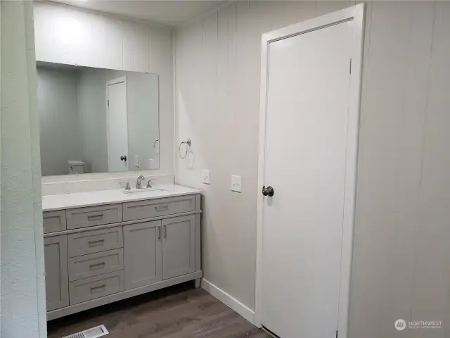 A Different Picture of the roomy Primary Master Bathroom Showing All New Cabinet Vanity, Counter Top, 2 Sinks, Faucets, Paint and Vinyl Plank Flooring.