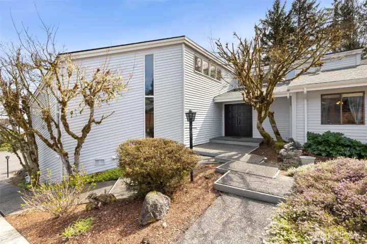 There’s a strong first impression here, and it sticks. The entry has that low, tiered approach that feels architectural without trying too hard, paired with a solid wood double door that instantly sets the tone. The exterior was freshly painted a few years ago in a warm, creamy neutral that feels both classic and right in step with today’s palette. A covered entry gives you options, a couple of chairs, seasonal decor, or a welcoming setup that stays protected from the weather. The landscaping is already established, so you’re not starting from scratch, and come spring, this whole front yard starts to bloom and fill in with color. It’s the kind of curb appeal that feels grounded, cared for, and ready to enjoy.