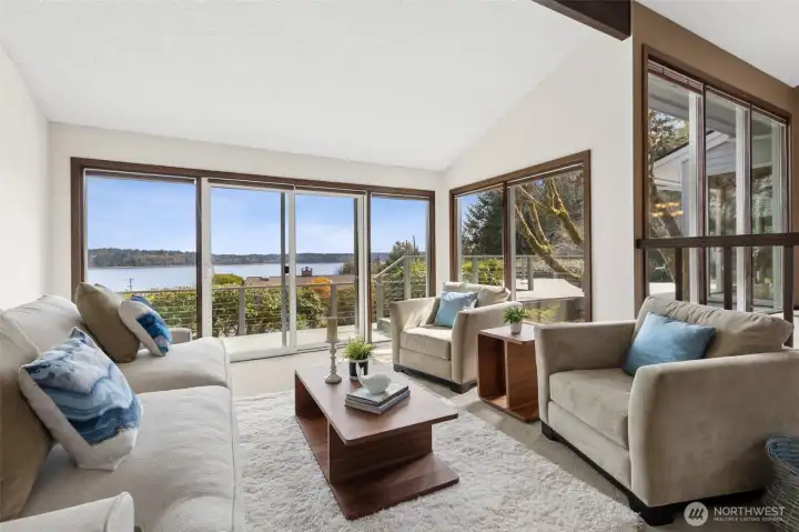 From this corner, it becomes clear just how much glass this space really has. Windows wrap around the living room, flanking the large sliding door and continuing onto the adjacent wall, creating a wide, uninterrupted sweep of the deck and water beyond. It’s layered, not just one focal point, but multiple angles that keep pulling your eye outward. You even catch the upper windows from the dining area above, adding another dimension of light and connection between spaces. While this isn’t direct waterfront, the view absolutely delivers, giving you that open, expansive feel without the maintenance that sometimes comes with it.