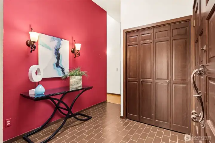 A warm, inviting first impression with just the right amount of character. The brick-style paver tile underfoot sets a grounded tone, while the accent wall in a rich terracotta hue adds depth and warmth without overpowering the space. It’s a natural landing zone when you walk in, with a large coat closet tucked behind wood bifold doors to keep things organized. The front door is a standout, solid wood with a beautifully detailed, scrolled handle that feels like a nod to the home’s original era in the best way. Vaulted overhead, the space feels open and airy, but still anchored with that vintage charm that gives it personality.