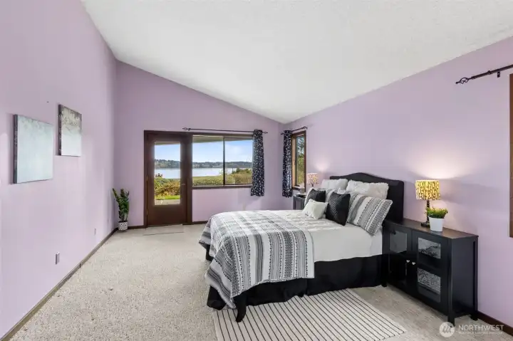 Waking up to this view is a pretty strong selling point. The primary suite carries those vaulted ceilings through, giving the room a sense of openness that pairs nicely with the water just beyond the window. A hinged door with a full mirrored panel reflects the light and keeps the view uninterrupted, which is a thoughtful detail you don’t always see. There’s plenty of space here for a king bed along with additional furniture, so it doesn’t feel tight or overfilled. The soft carpeting underfoot adds comfort, making this room feel like a true place to unwind at the end of the day.