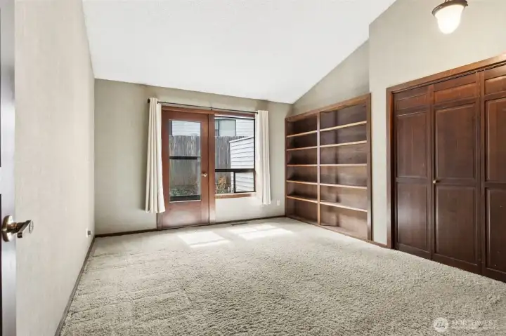 The second bedroom brings a lot more to the table than just a bedroom. With its own exterior door and a large window, it has that added flexibility that makes it perfect for guests, a home office, or even a private studio-style setup for multigenerational family members. Built-in bookshelves add both function and character, giving you a ready-made spot for storage or display without needing extra furniture. The vaulted ceiling keeps it feeling open, while the warm tones and soft carpeting make it comfortable and easy to settle into. A spacious closet rounds it out, making this a room that can easily adapt to whatever you need it to be.