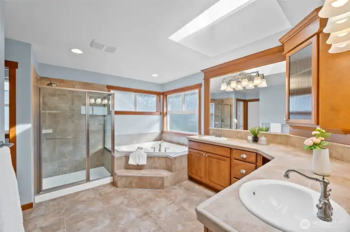 Stunning, luxurious en-suite primary bathroom filled with natural light from a skylight and abundant windows and storage. There is a convenient linen closet tucked to the left.