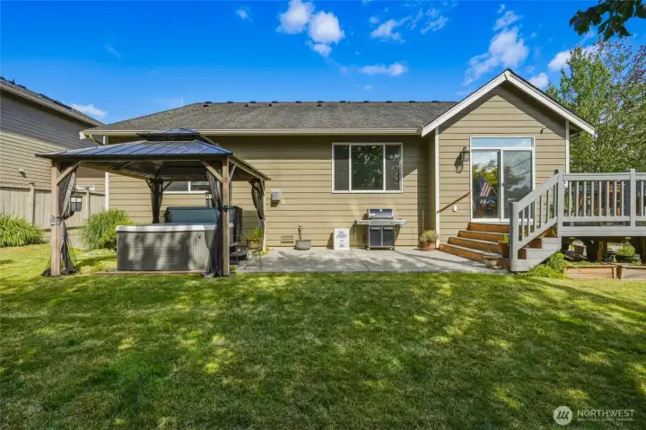 Beautiful backyard with a spacious deck, gazebo-covered hot tub, patio, and lush lawn.