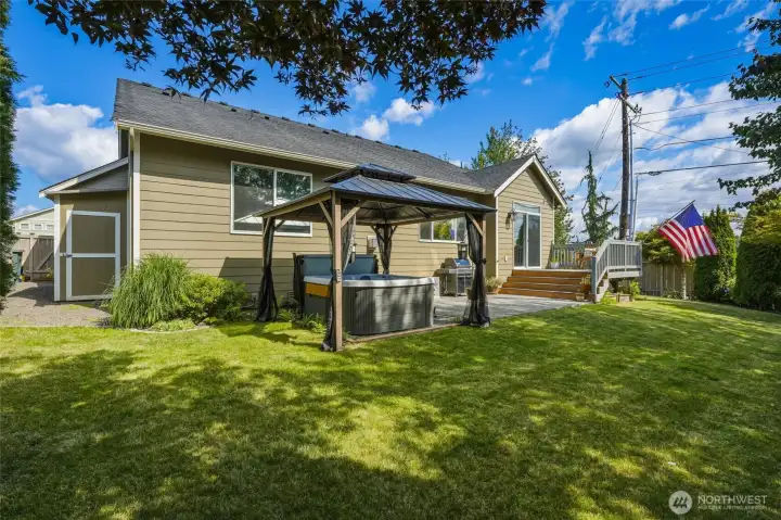 Expansive, fully fenced backyard featuring a spacious lawn, entertaining deck, gazebo-covered hot tub, and patio.