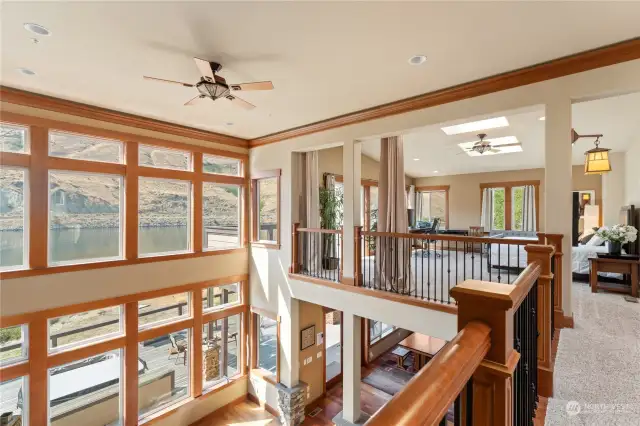 View of upper level catwalk overlooking the living room w/ vaulted ceilings and oversized windows overlooking the Columbia River and upper level loft office w/ extra sleeping area.