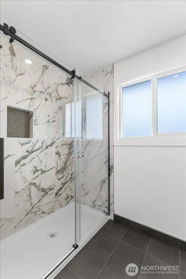 Primary bathroom with oversized walk in shower with gorgeous tile work and tile flooring.