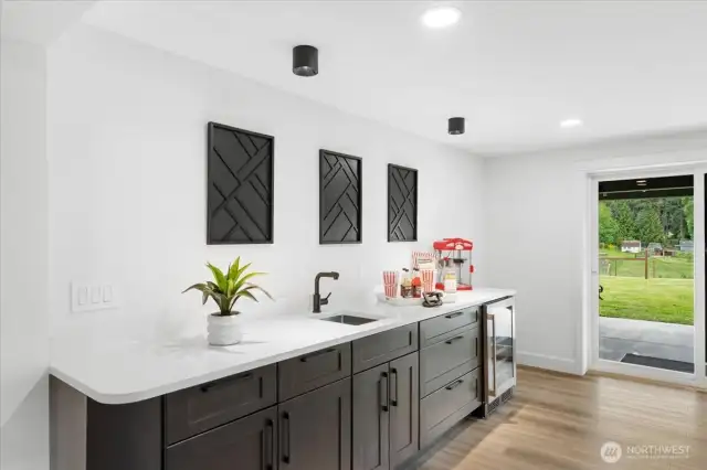 Wet bar in game room with beverage fridge and room for a full sized fridge.