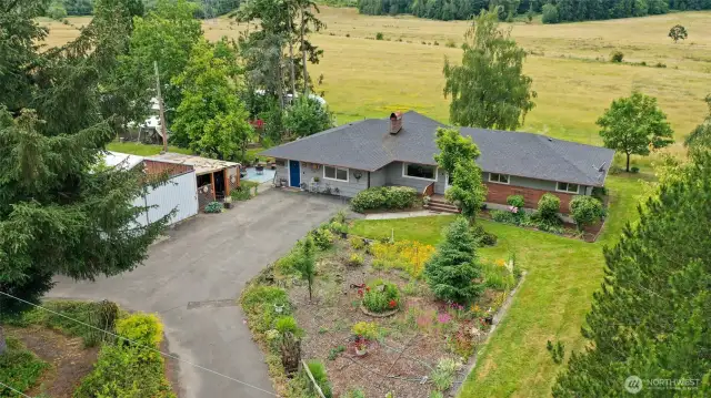 The home features a circular driveway, offering convenient in-and-out access. Pictured is an aerial view showcasing the home, and first shop, another shop is beyond the trees. That open acreage behind the home is part of the lot.
