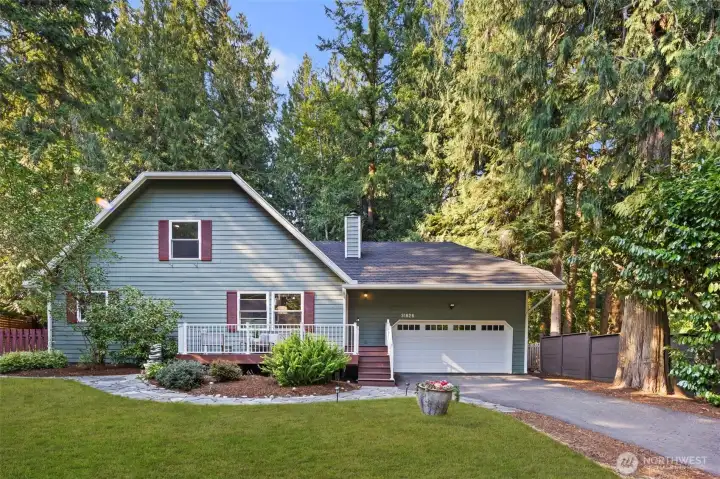 This charming home instantly feels inviting with its classic front porch, cheerful shutters, and lush landscaping. Nestled among tall evergreens, it exudes a cozy, homey feel that’s both welcoming and serene.
