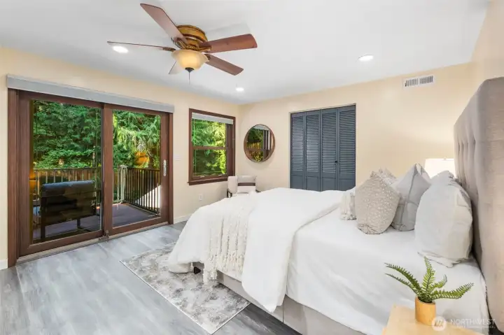 Across the hallway, the spacious primary bedroom features a wood ceiling fan that complements the rich wood casings around the window and sliding glass door. Step directly onto the private deck through the sliding door, surrounded by forest views, perfectly hidden view by a hill and wooded forest.