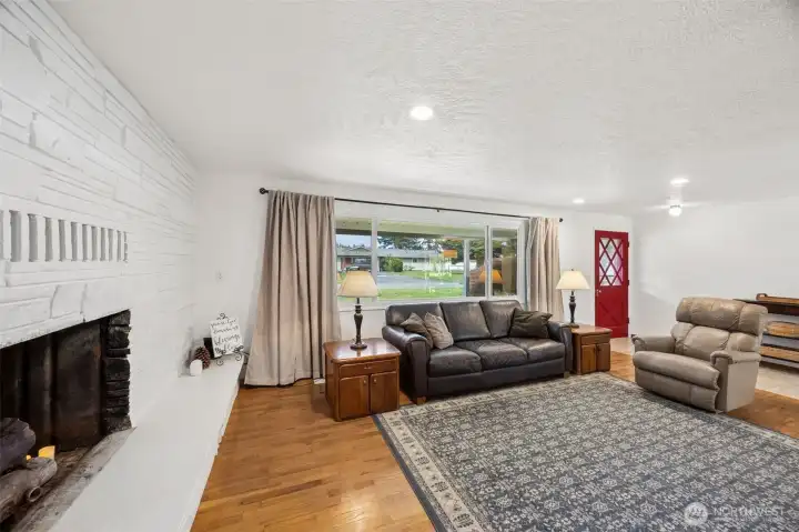 The big picture window looks out over the covered front walkway and brings in beautiful light, while giving you a better sense of the full width of the room and just how much gorgeous oak flooring runs across it. Then there is that full wall stone fireplace, and it is absolutely the architectural anchor of the space. While there is not a functioning insert in place at the moment, it is stubbed and capped for propane, with about $1,000 worth of propane currently in the tank included with the sale. Sellers also added a new chimney cap and completed repairs to the top brickwork and chimney flashing, which speaks to care in both the visible and not-so-visible details.