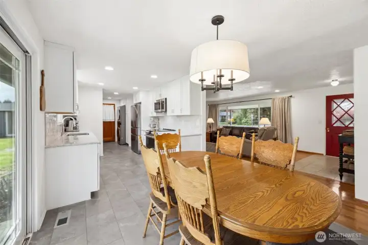 The gray-toned luxury vinyl flooring has a subtle stone-like look that brings texture and a little edge, balancing beautifully against the warm oak hardwoods in the living room. Fresh white paint throughout keeps everything bright and lifted, letting natural light bounce from room to room and making the whole home feel open and inviting. From here you can also appreciate the flow, from dining to living, down through the kitchen and out the side door.