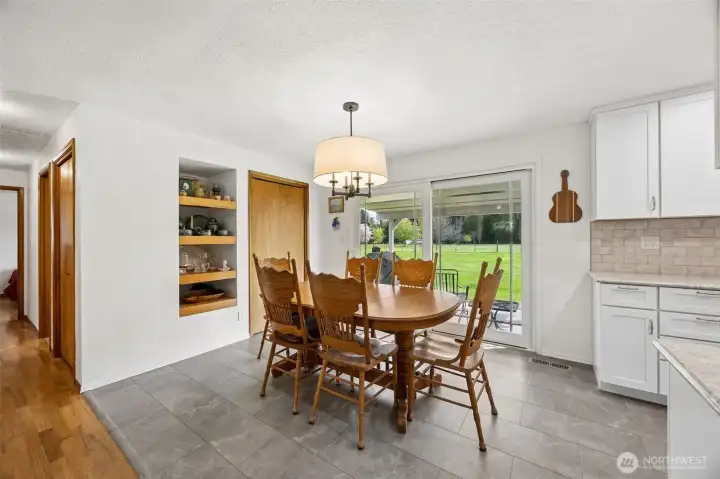 The drum chandelier gives the room presence without overpowering it, and those custom open shelves add a layer of character that feels both collected and practical. It is storage, styling and conversation piece all in one. Right beside it, the coat closet quietly adds another smart touch. The luxury vinyl tile in the kitchen and dining areas was a very savvy choice too, waterproof, durable and ready for real life on acreage where things occasionally come in from outdoors. And that oversized sliding glass door is a star here, opening wide to the covered porch and creating that easy pull toward the land beyond.