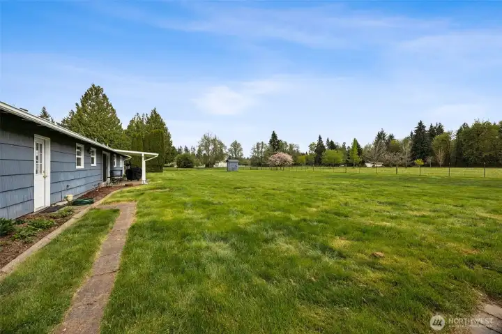 You can see the additional exterior door off the laundry near the kitchen, which is a very handy connection for daily life, especially on acreage. This view also shows the septic and drainfield positioned close to the house in this backyard section, which is actually a meaningful advantage. It keeps those systems out of conflict with the existing outbuildings and away from the heavier traffic of the gravel drive and equipment access. Smart placement like that matters. And beyond that practical layer, look at the space. Wide open lawn ready for gardens, play areas, sport setups, outdoor entertaining, whatever vision wants to land here.
